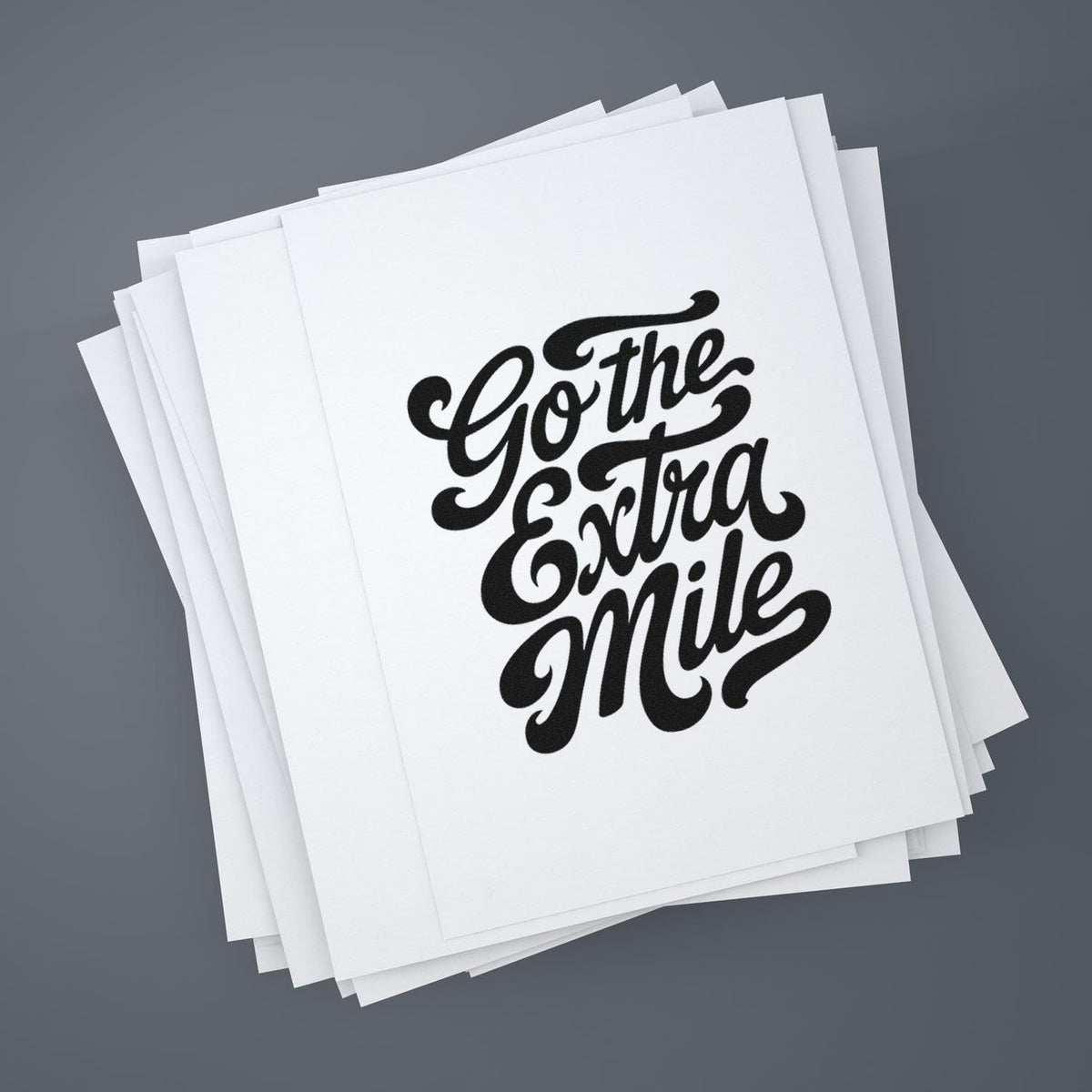 Stack of white stamp and seal sheets with black script reading Go the Extra Mile on a gray background.