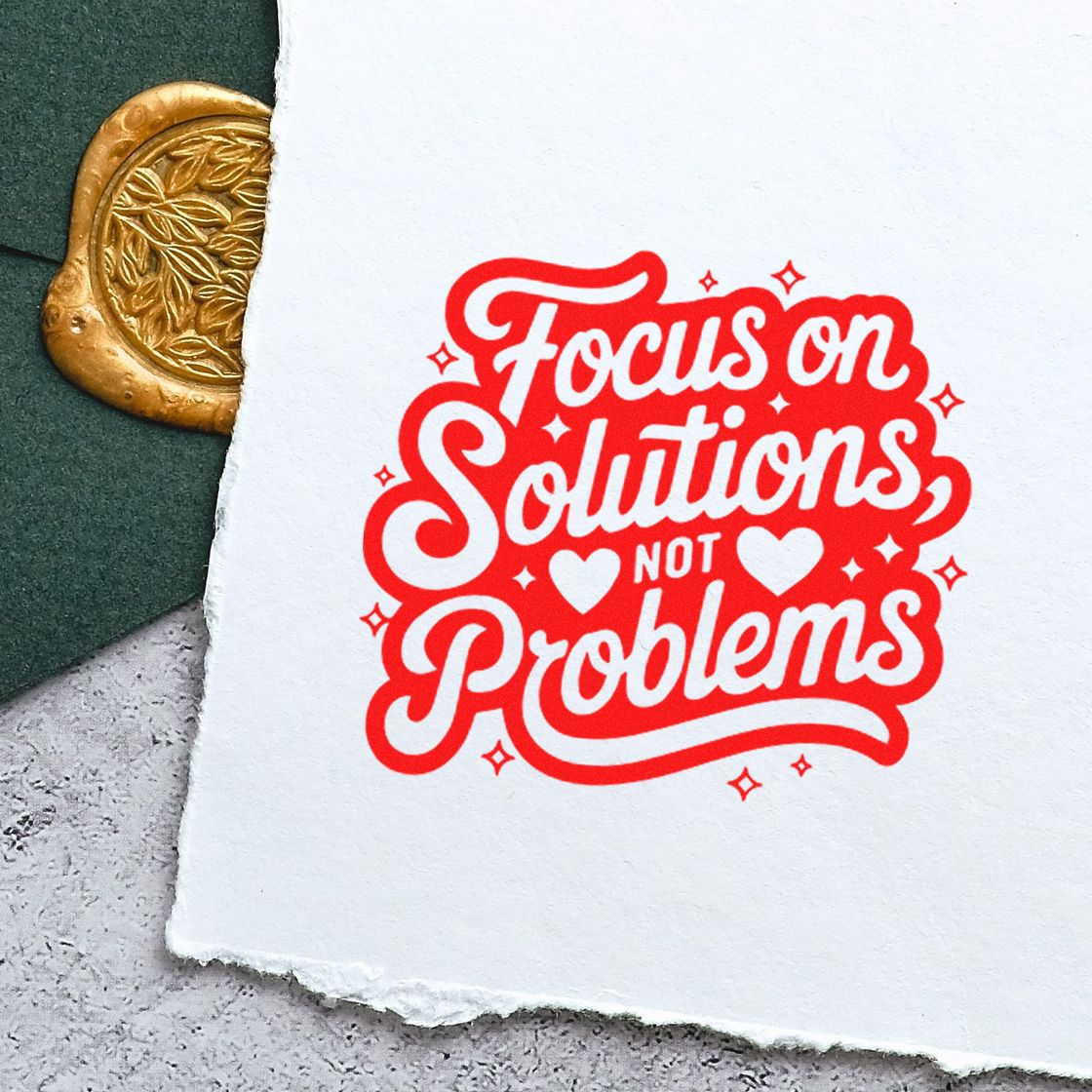 Red stamp on white paper reading Focus on Solutions Not Problems, beside a gold embossed seal on dark green background.