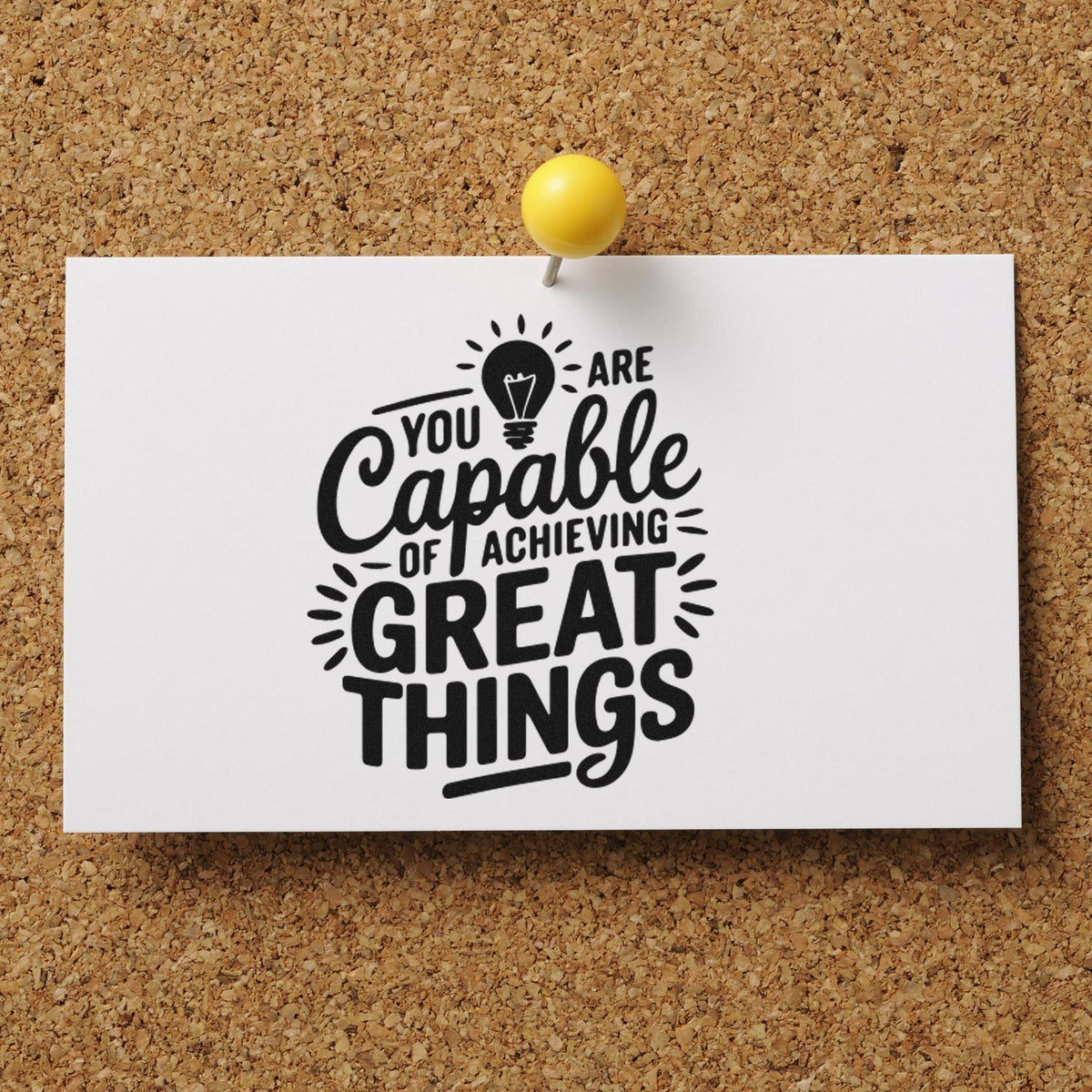 White custom stamp sample with black motivational lettering, pinned by a yellow pushpin on a corkboard.