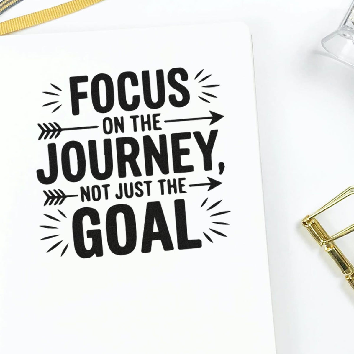 Black motivational stamp on white paper with arrow accents: Focus on the journey, not just the goal, beside gold seal tools.