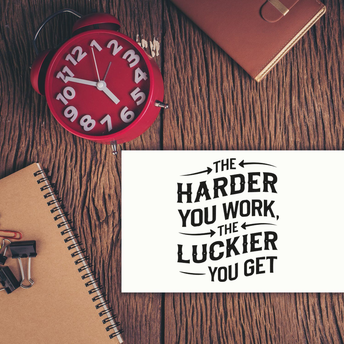 Black rubber stamp/seal impression on white card beside a red alarm clock, notebook, and leather journal on rustic wood.