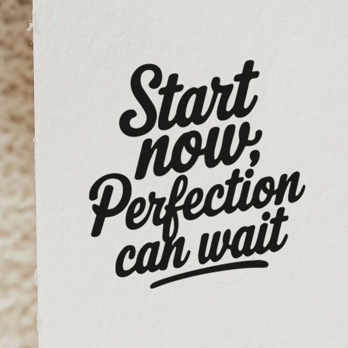 Black script stamp on white paper reading Start now, perfection can wait, a stamp and seal product.