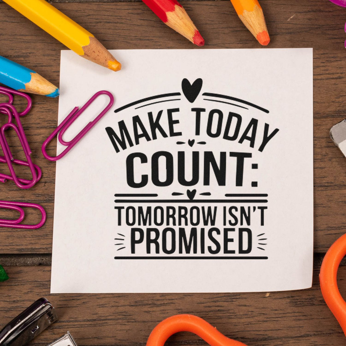 Black motivational stamp and seal design on white paper, with hearts, colorful pencils, and pink paperclips on a wood desk.