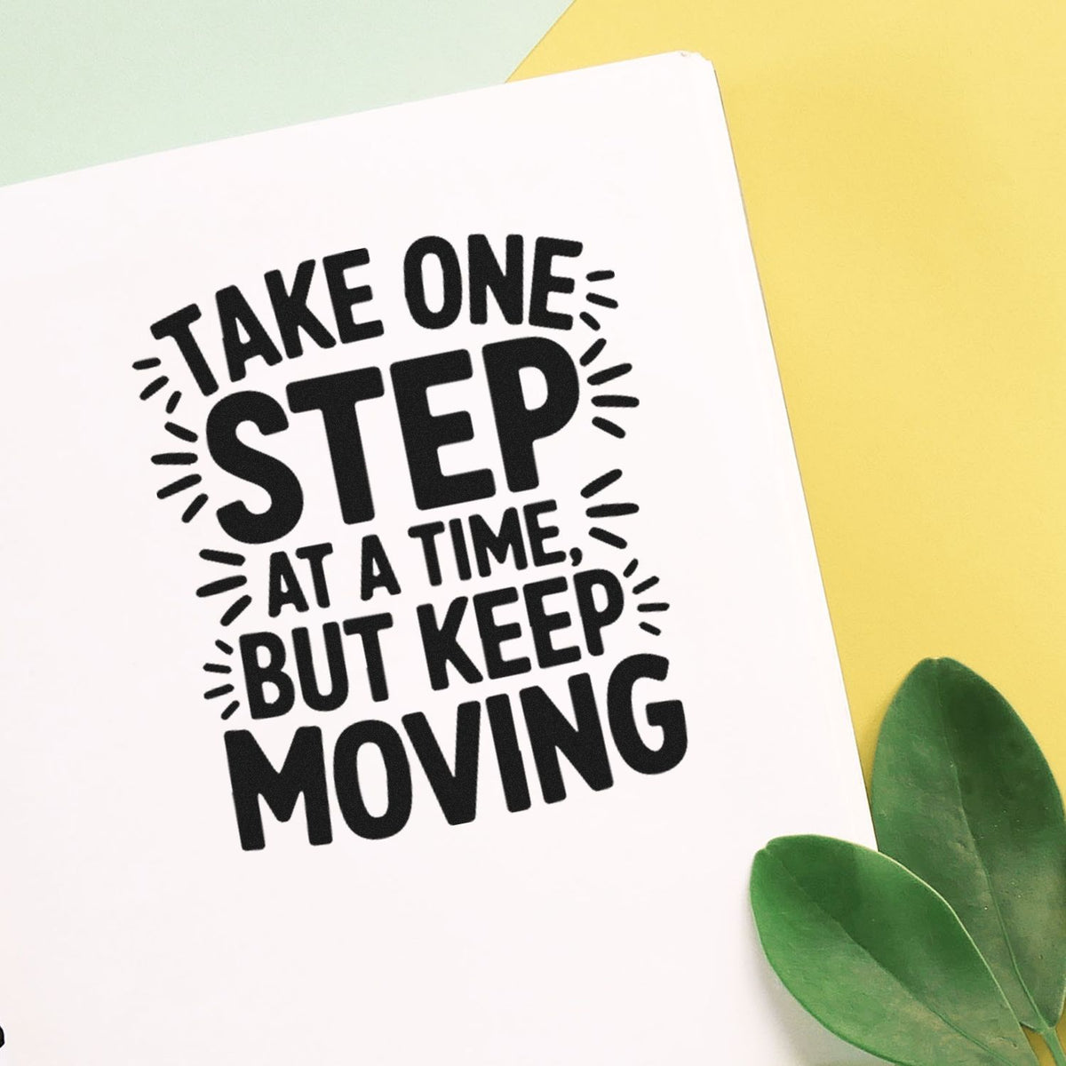 Bold black rubber stamp reading Take one step at a time, but keep moving on white card, with yellow background and green leaves.