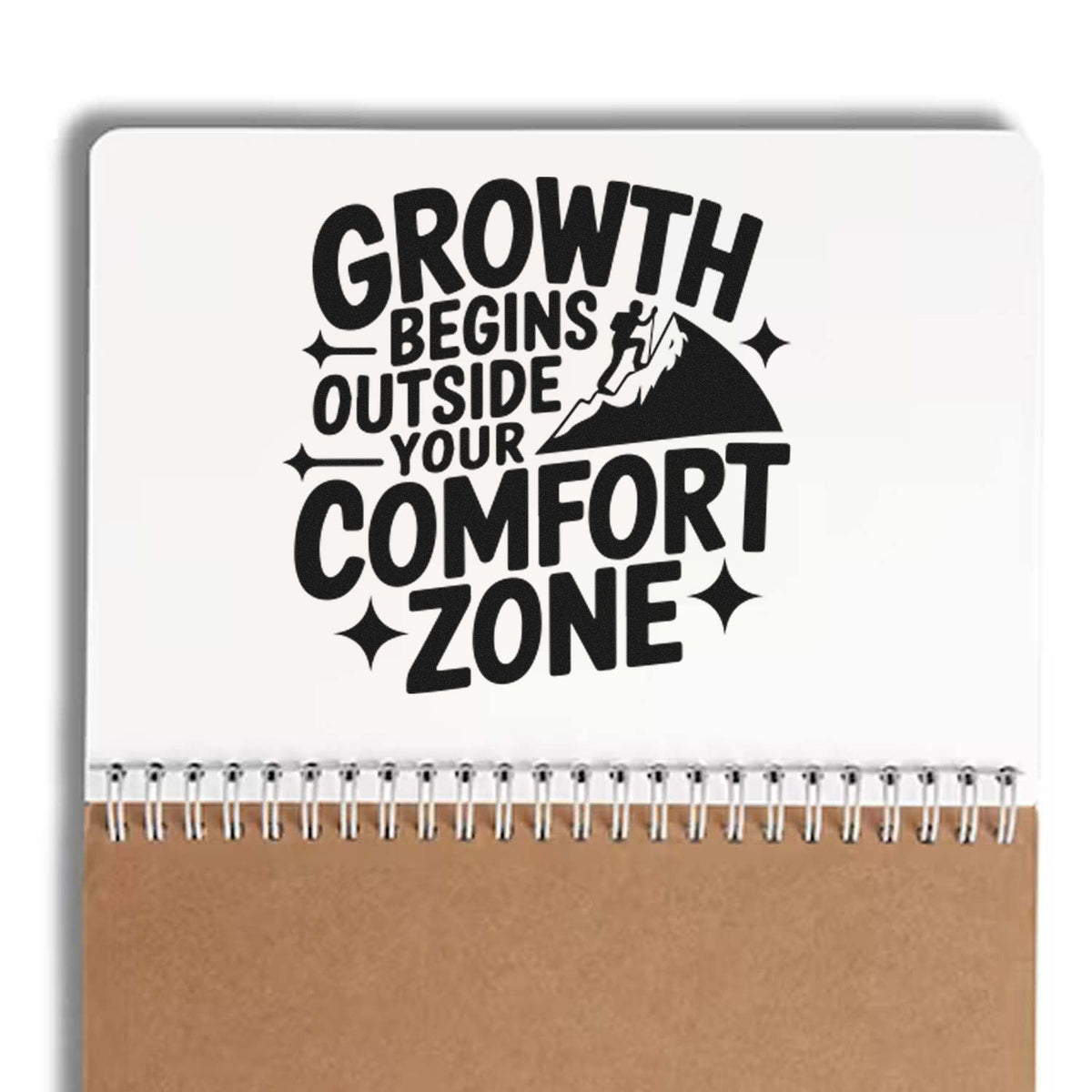 Black stamp-style design on white notebook cover, tan spiral bottom, mountain climber, text: Growth Begins Outside Your Comfort Zone.
