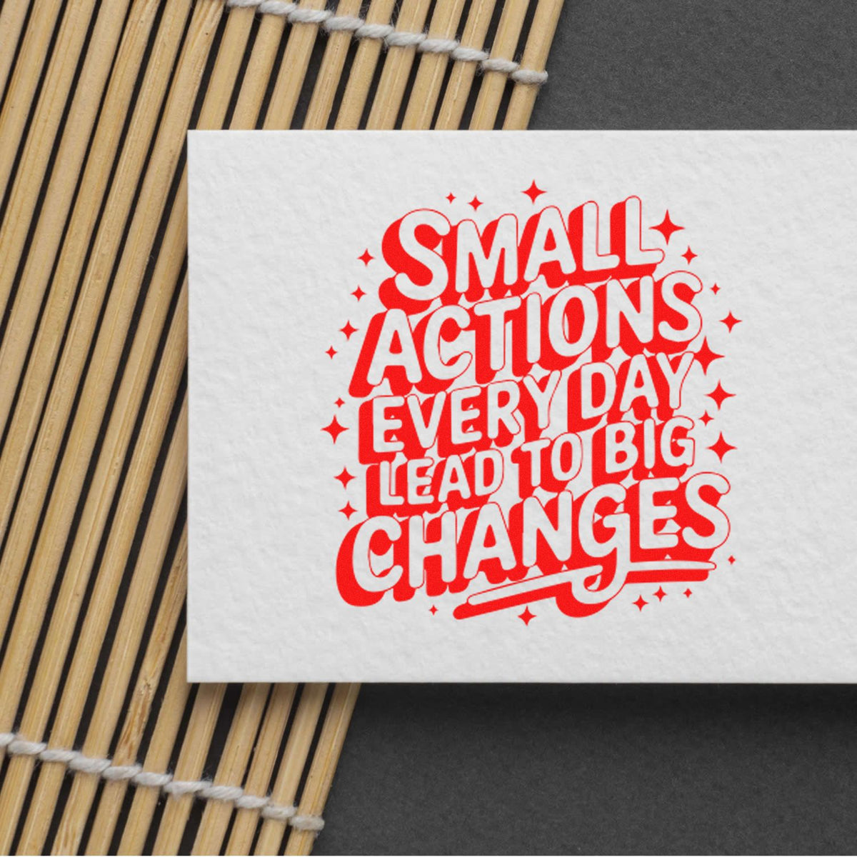 White stamp and seal card with bold red retro text, Small Actions Every Day Lead to Big Changes, on a bamboo mat.