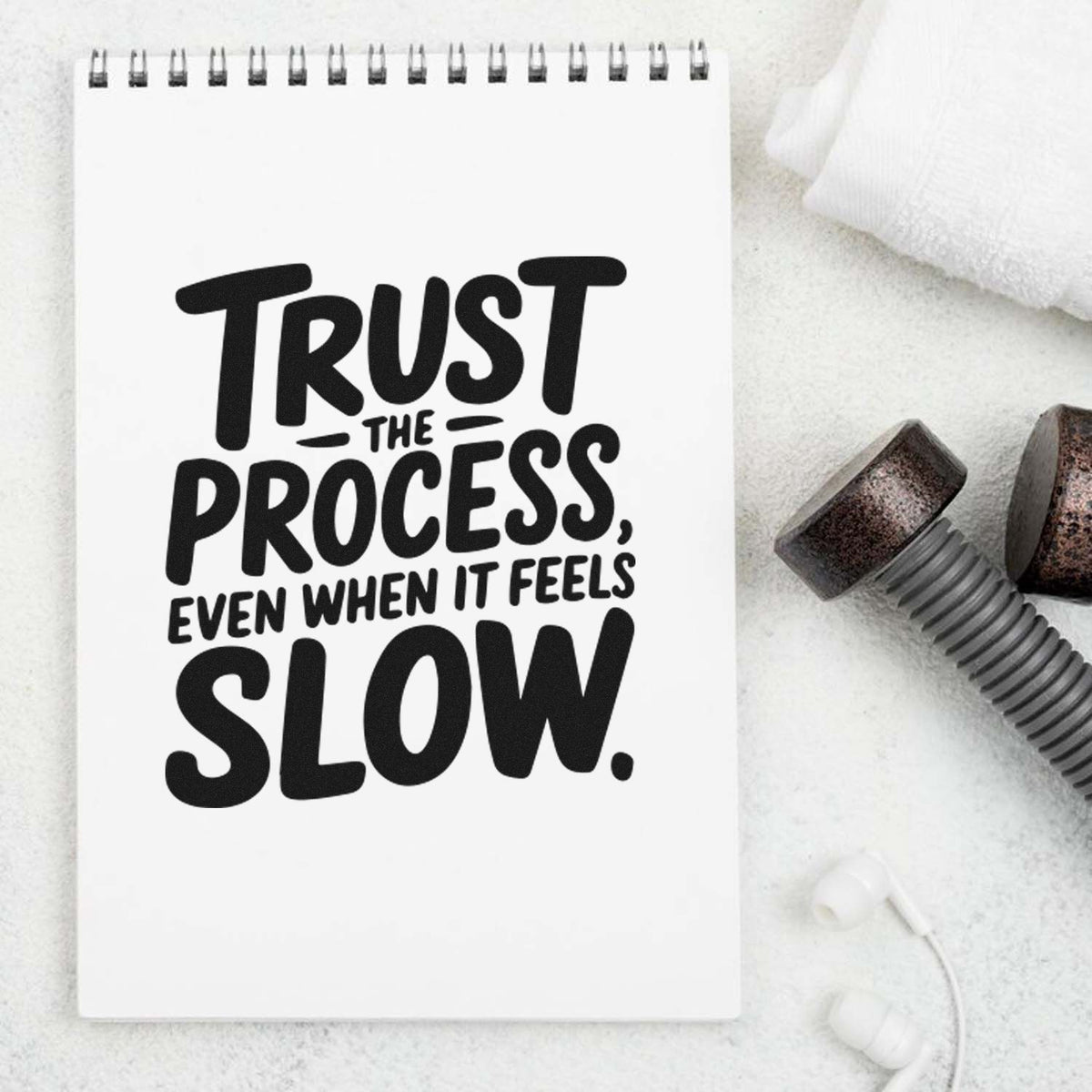 White spiral notepad with black stamp-style quote Trust the process, even when it feels slow, beside dark rubber stamp seals.