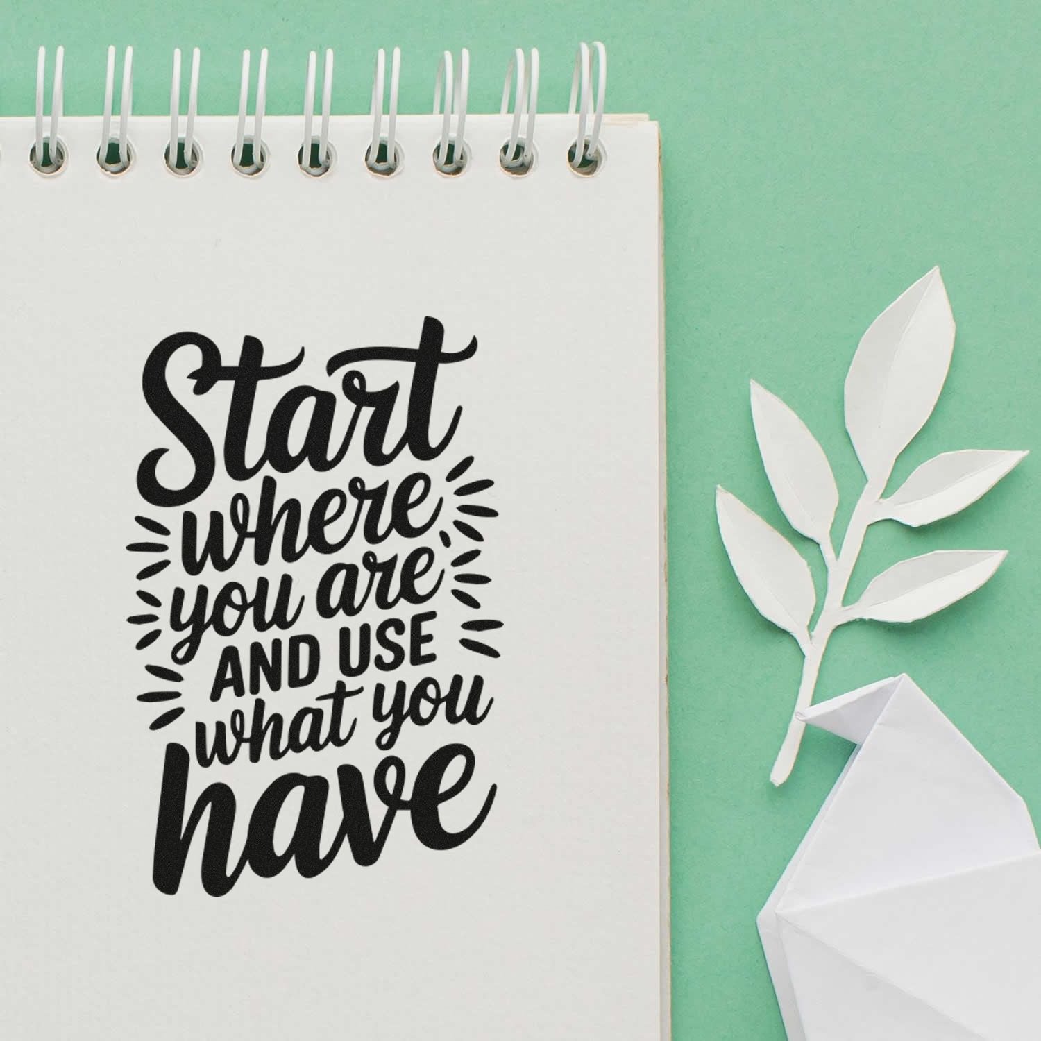 Black script stamp on white spiral notebook, with white paper leaf seal and folded paper seal on mint green background.