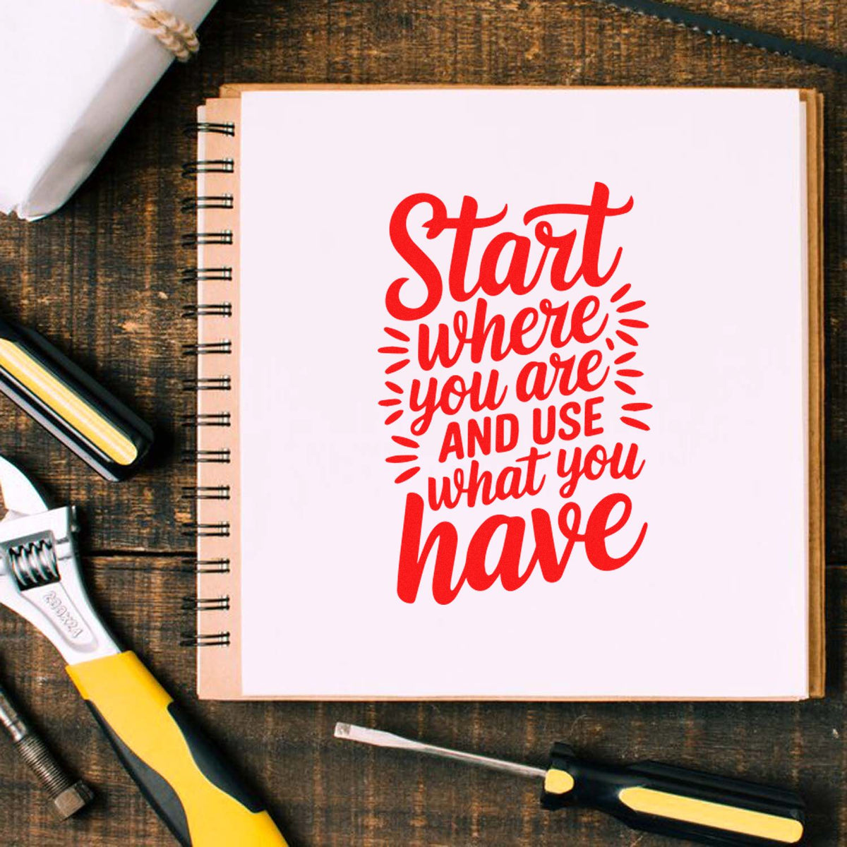 Red motivational stamp design on a white notebook, with black-and-yellow stamp and seal tools on a rustic wood desk.
