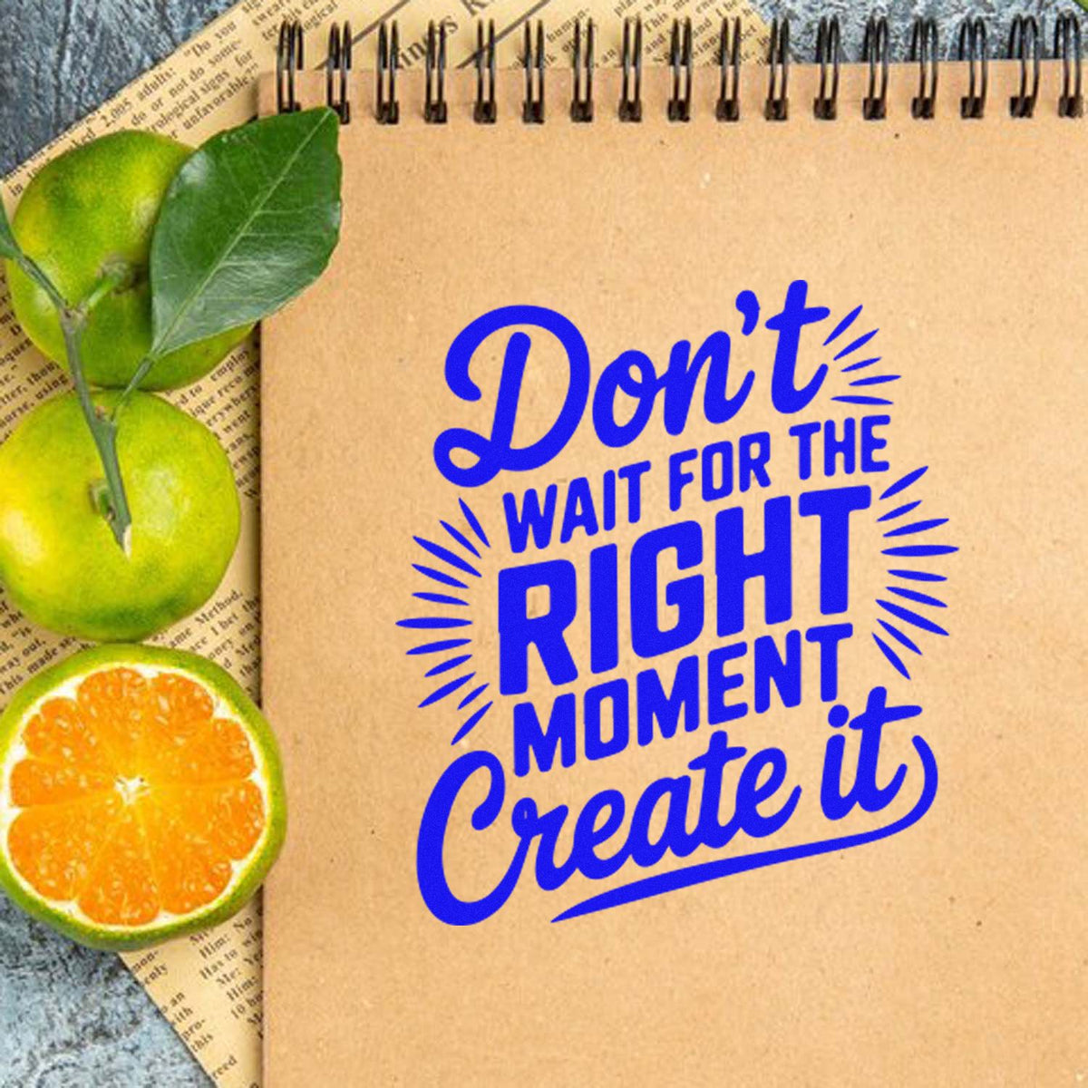Blue stamp and seal design on kraft notebook with citrus slices and green leaves, reading Dont wait for the right moment, create it.