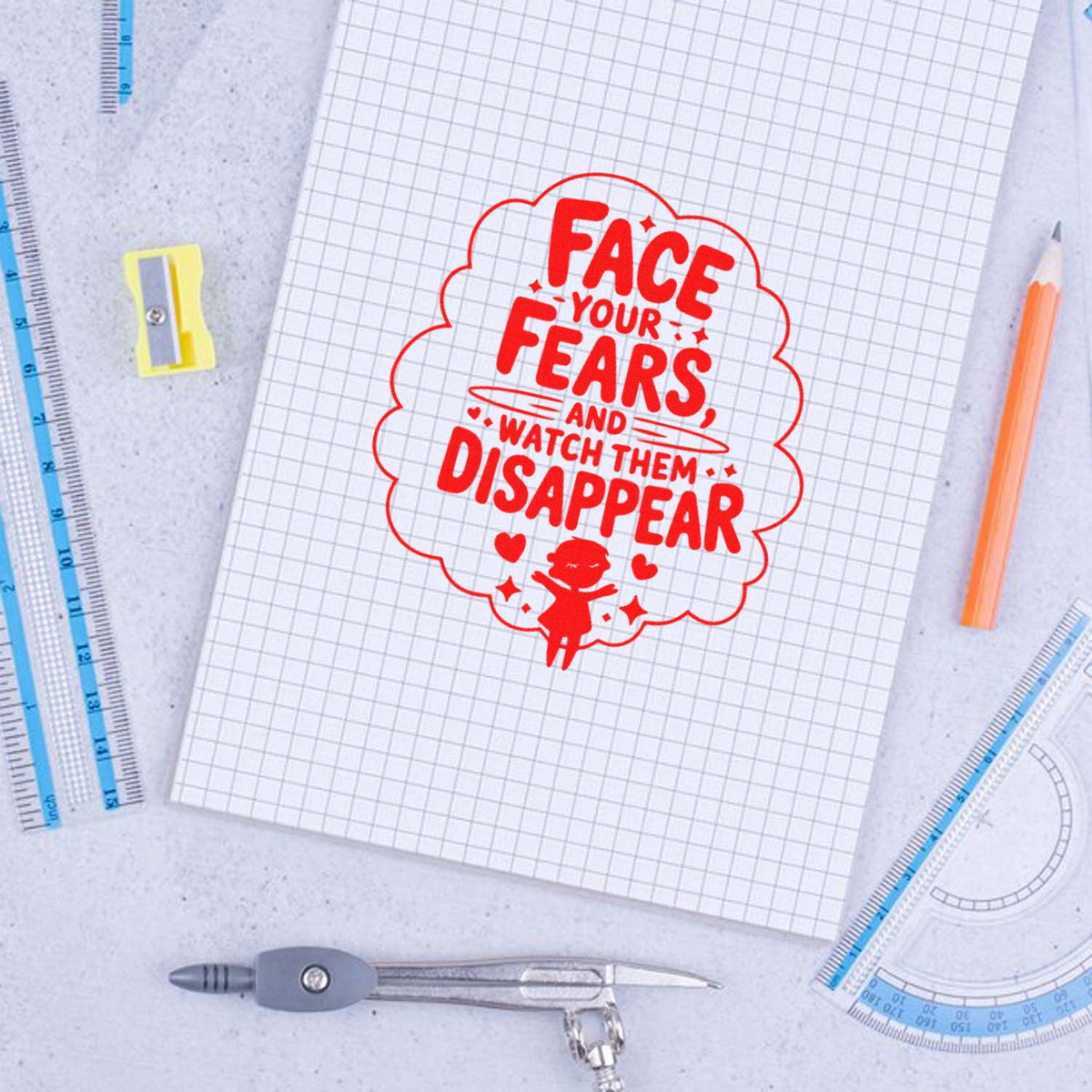 Red custom stamp seal with Face Your Fears, and Watch Them Disappear on graph paper, surrounded by rulers and pencil.