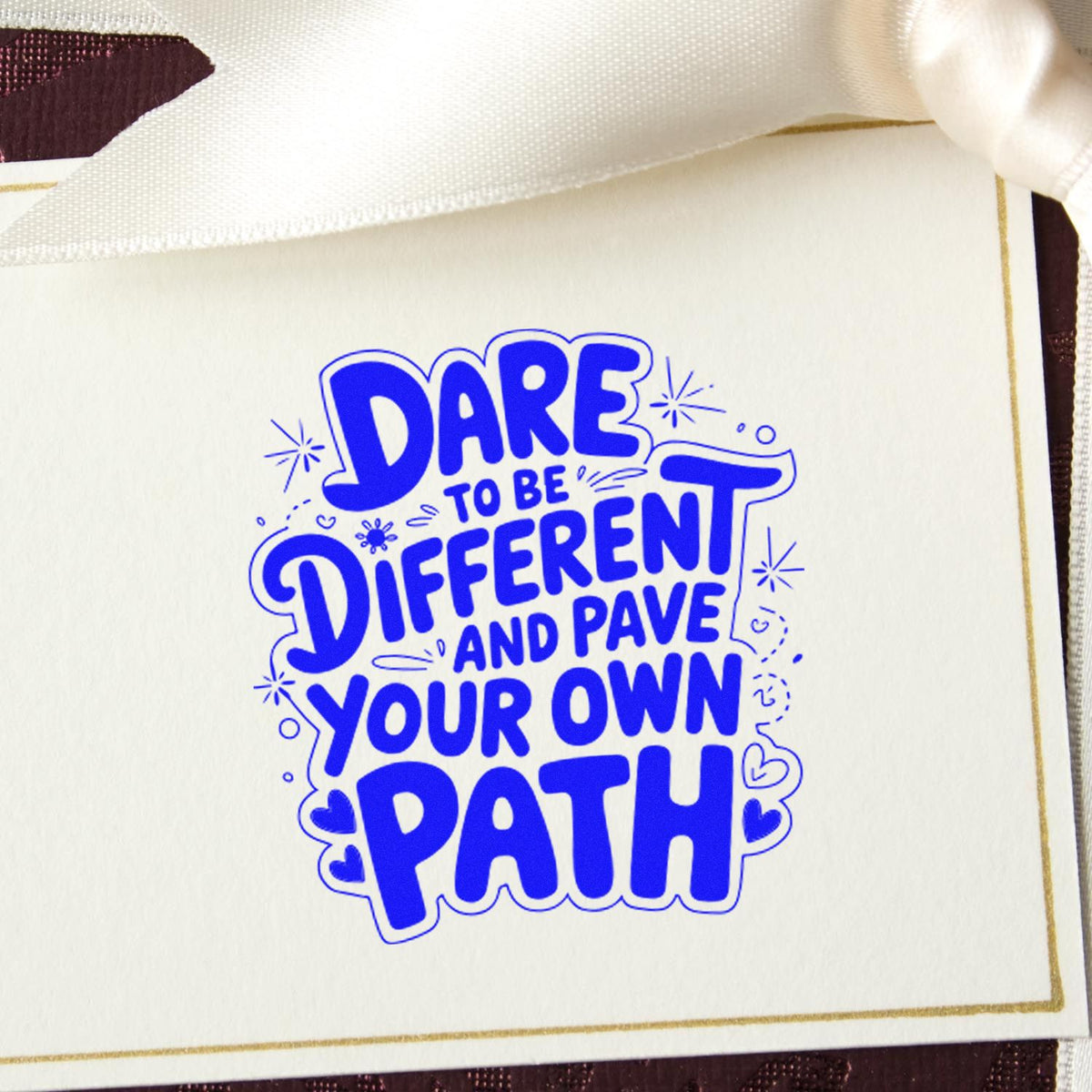 Blue stamp seal reading Dare to be different and pave your own path on a white card with gold border.