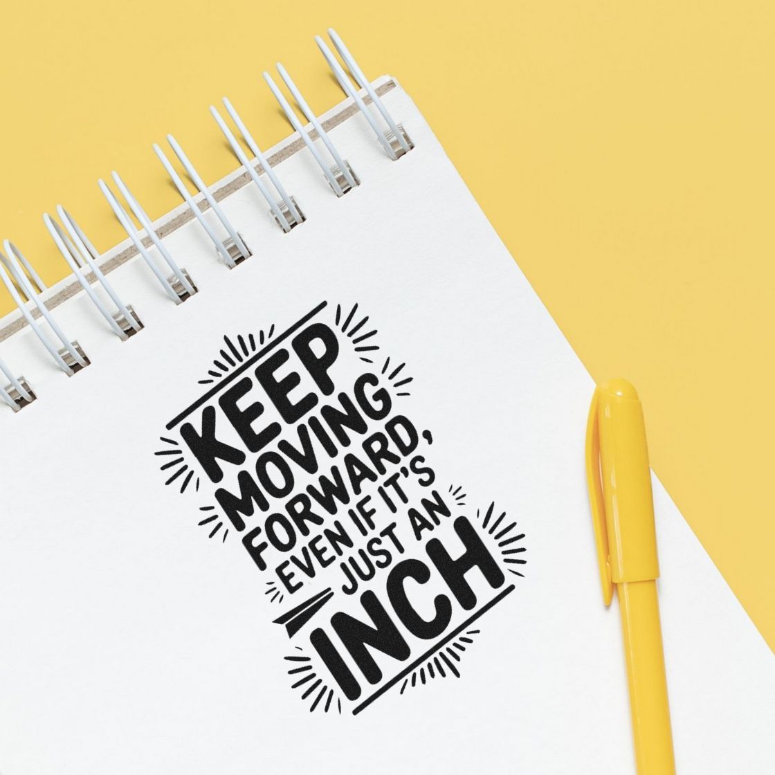 Black motivational stamp seal on white spiral notebook, reading Keep Moving Forward, Even if its just an inch, with yellow pen on yellow background.