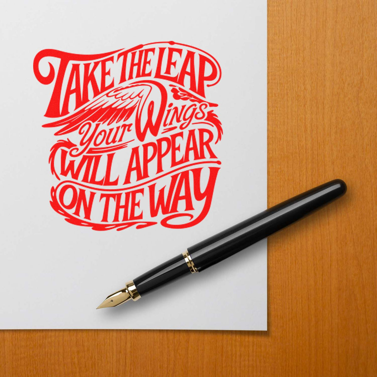 Red take-the-leap winged stamp seal beside a black and gold fountain pen on white paper over a wood desk.
