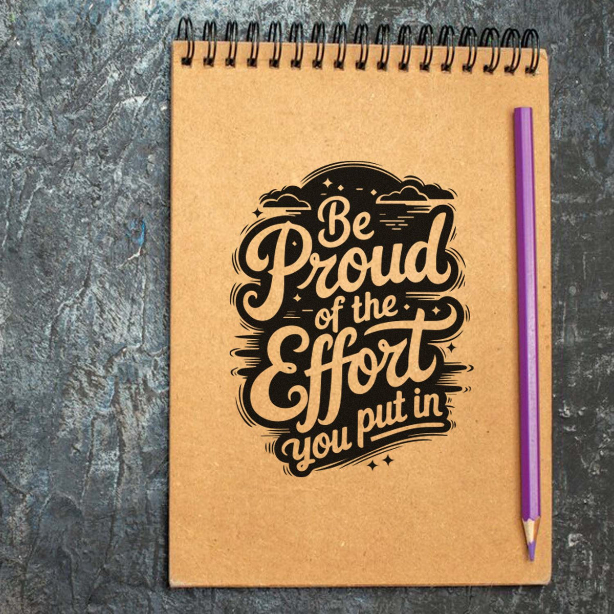 Kraft brown spiral notebook with a black stamped Be Proud of the Effort you put in design and a purple pencil.