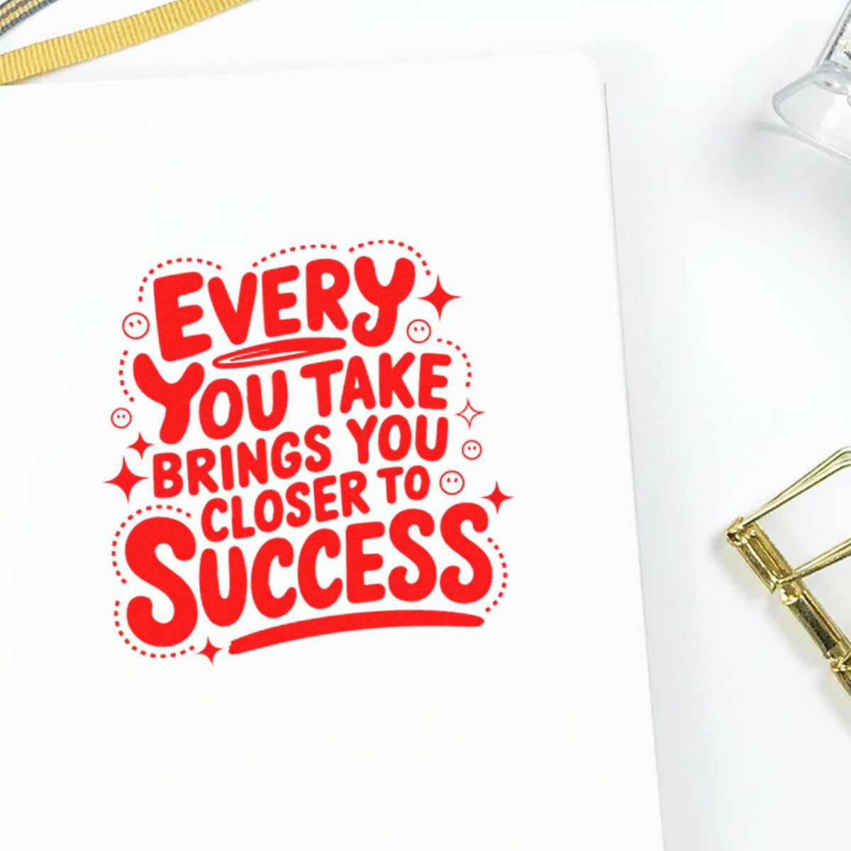 Red decorative stamp seal with motivational quote on white paper, accented by gold clip details