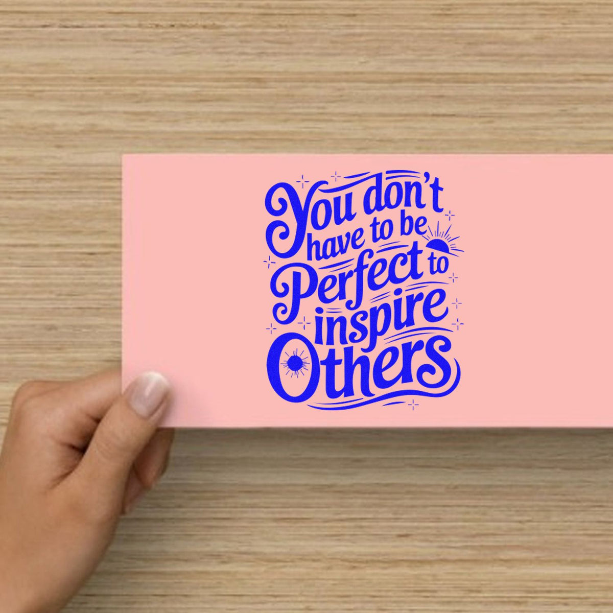 Pink stamp and seal card with bold blue quote, You dont have to be perfect to inspire others, held by a hand.