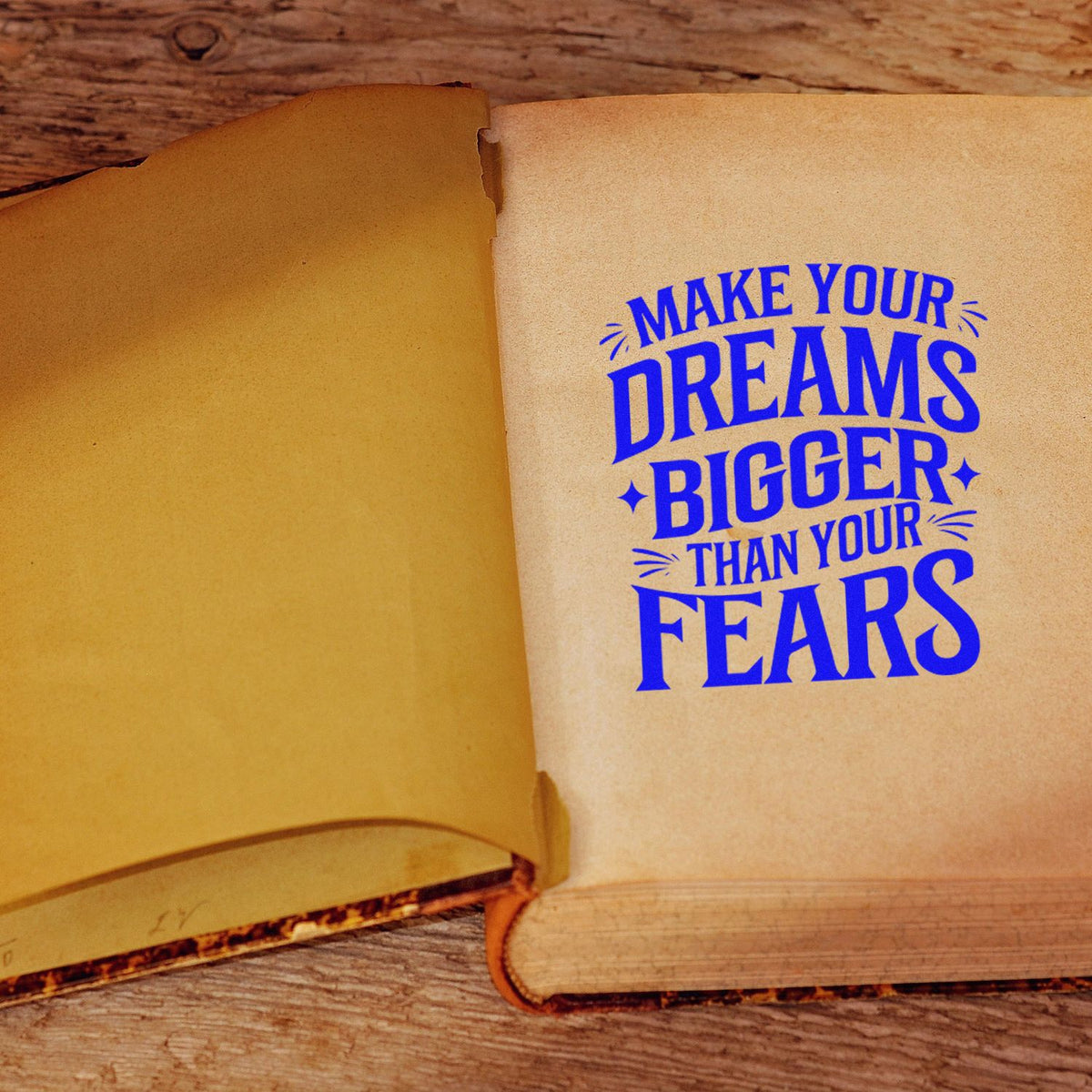Open vintage book with bold blue stamp-style seal reading Make your dreams bigger than your fears on tan pages.