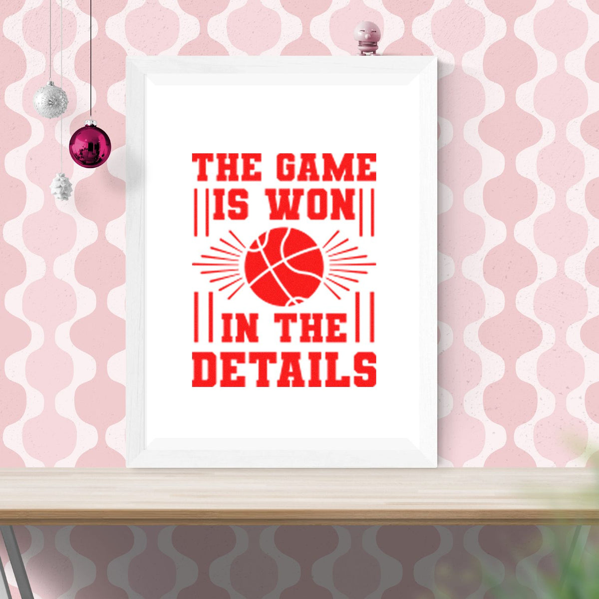 Framed stamp-style seal art with bold red basketball graphic and text The Game Is Won in the Details on pink wallpaper.