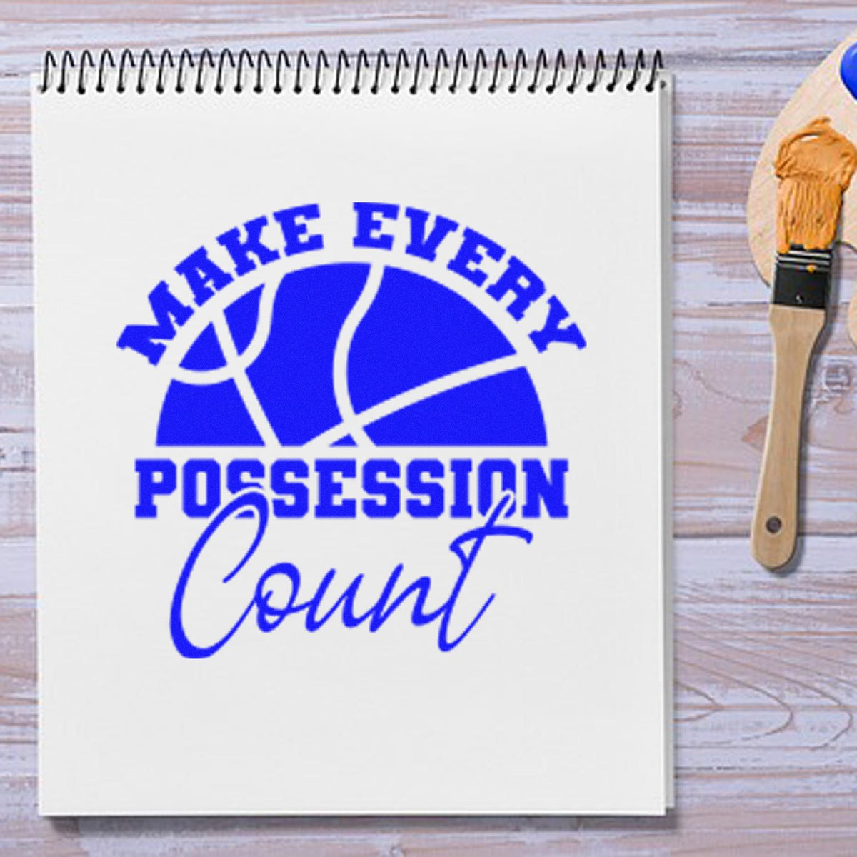 Blue custom stamp and seal with basketball graphic and slogan Make Every Possession Count on white notebook, wooden handle beside it.