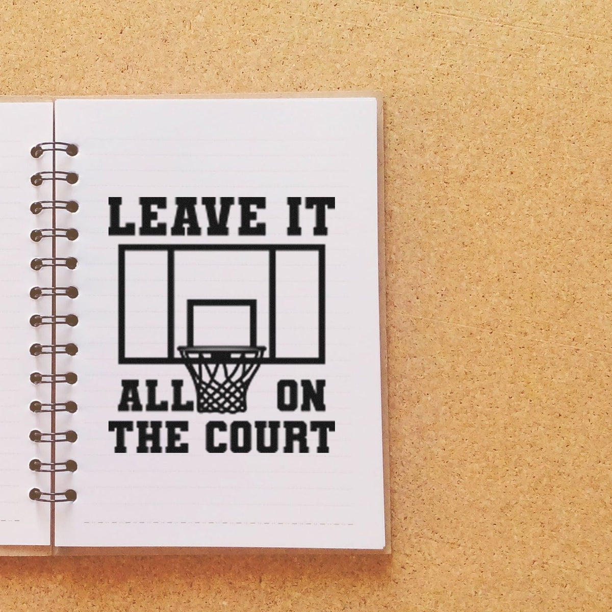 Black rubber stamp design on white notebook page reads LEAVE IT ALL ON THE COURT with basketball hoop graphic.