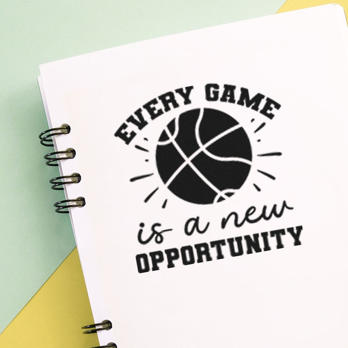 Black basketball stamp seal on white notebook page, reading Every game is a new opportunity, on mint green and yellow.