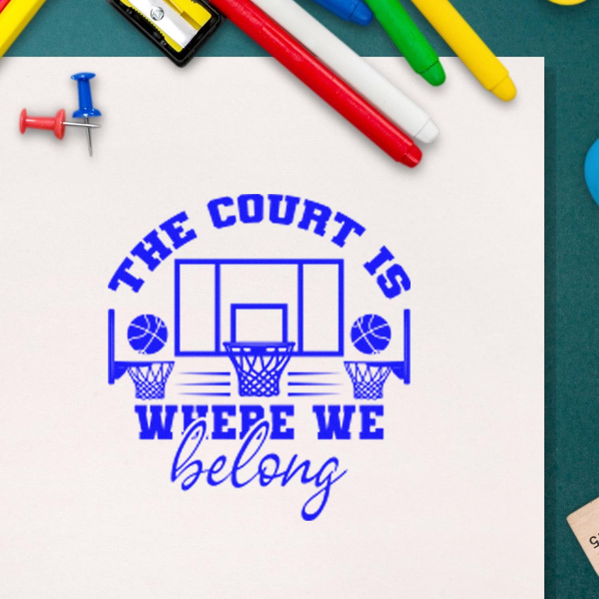 Blue basketball court stamp and seal reading The Court Is Where We Belong, with colorful markers and push pins.