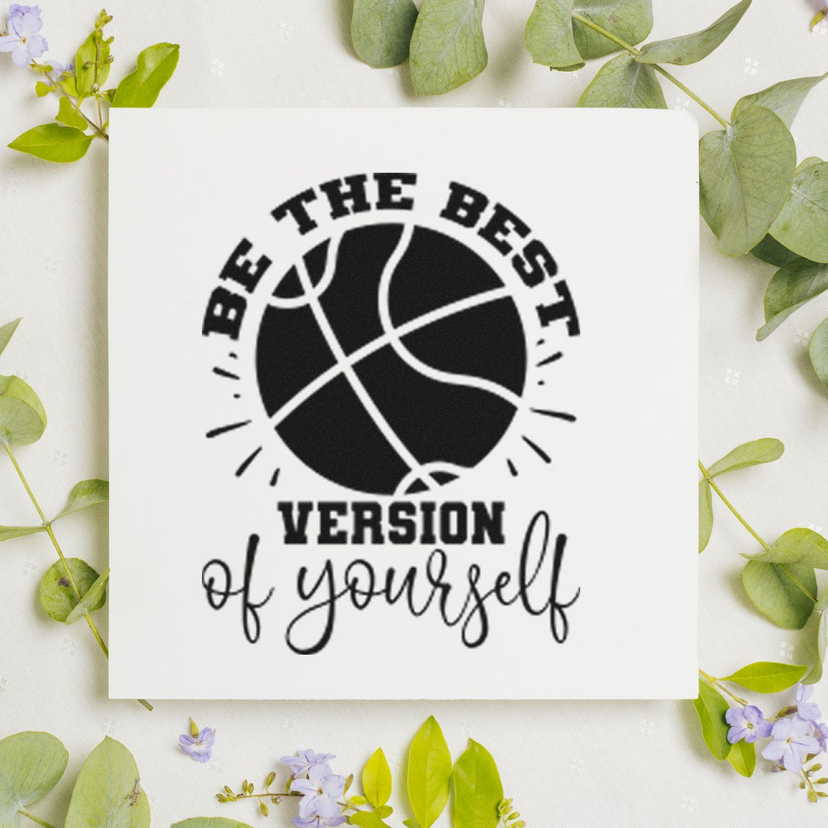 Black motivational stamp and seal with basketball graphic and text Be the best version of yourself on white, framed by green leaves.