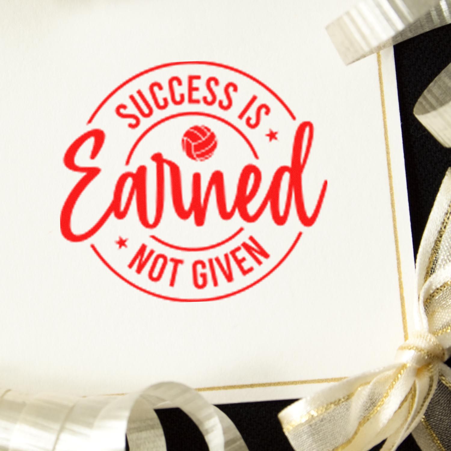 Red circular success stamp seal reading Success Is Earned, Not Given on white card with gold ribbon accents