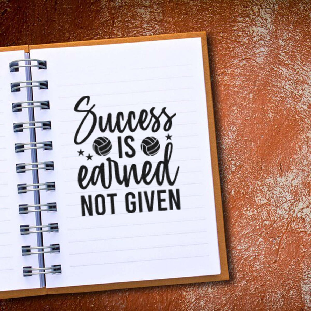 Black motivational stamp/seal reading Success is earned not given with volleyball icons on a white spiral notebook.