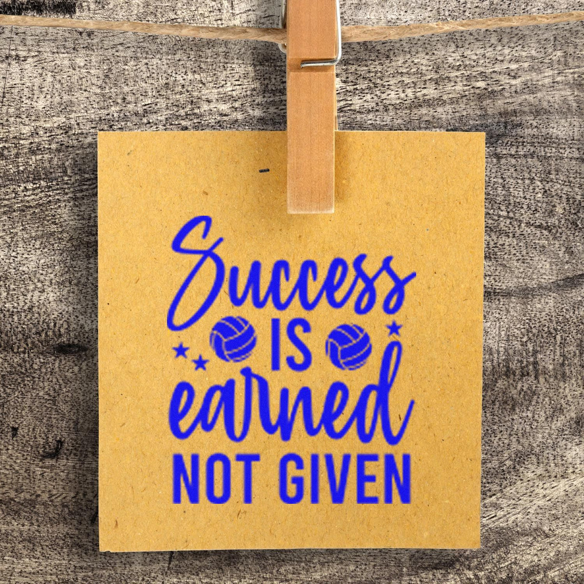 Blue custom stamp and seal on a yellow hanging tag reading Success is earned, not given, clipped with a wooden clothespin.