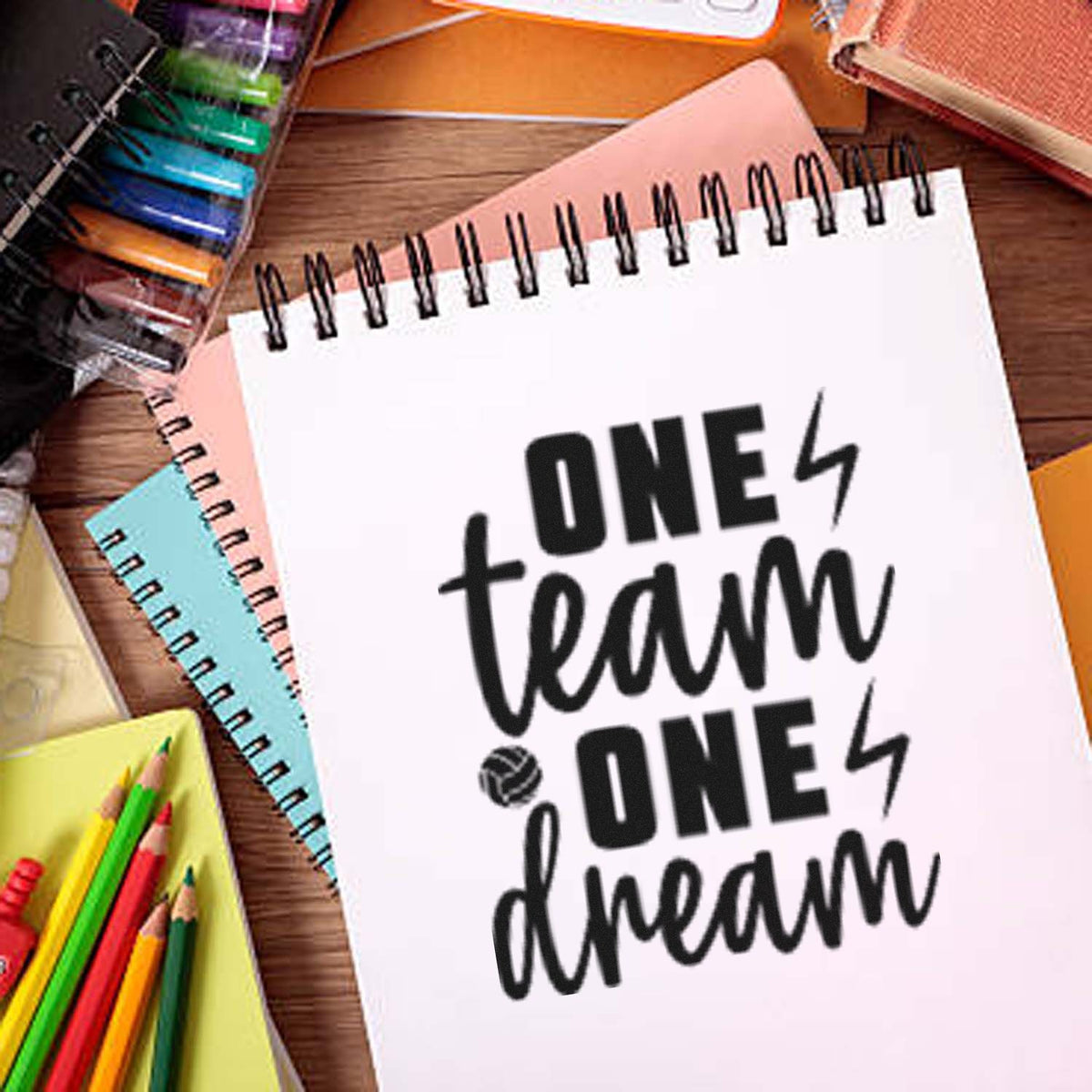 Black one team one dream stamp/seal on a white spiral notebook, surrounded by colorful stationery and notebooks.