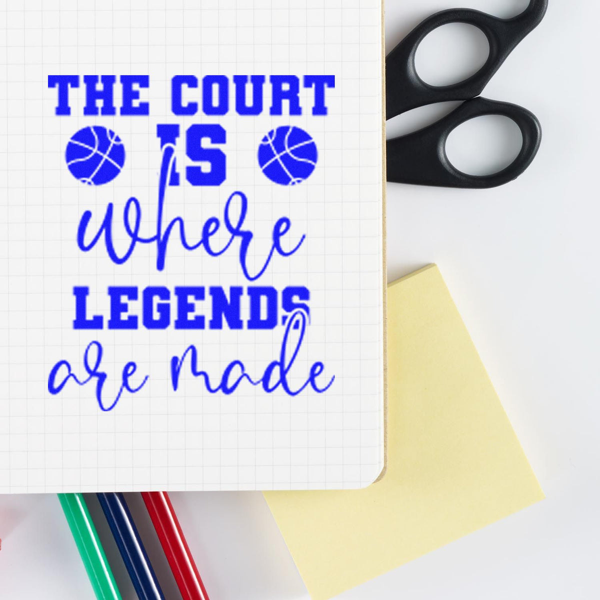 Blue custom stamp on graph paper reading The court is where legends are made, with black stamp handles, sticky note, and colored pens.