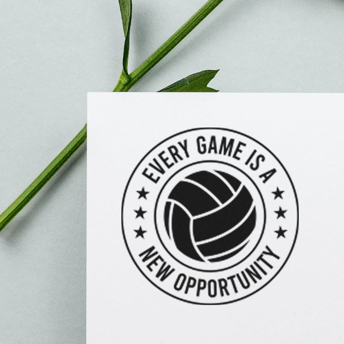 Black volleyball stamp seal reading Every Game Is a New Opportunity on white card, with green stem background.