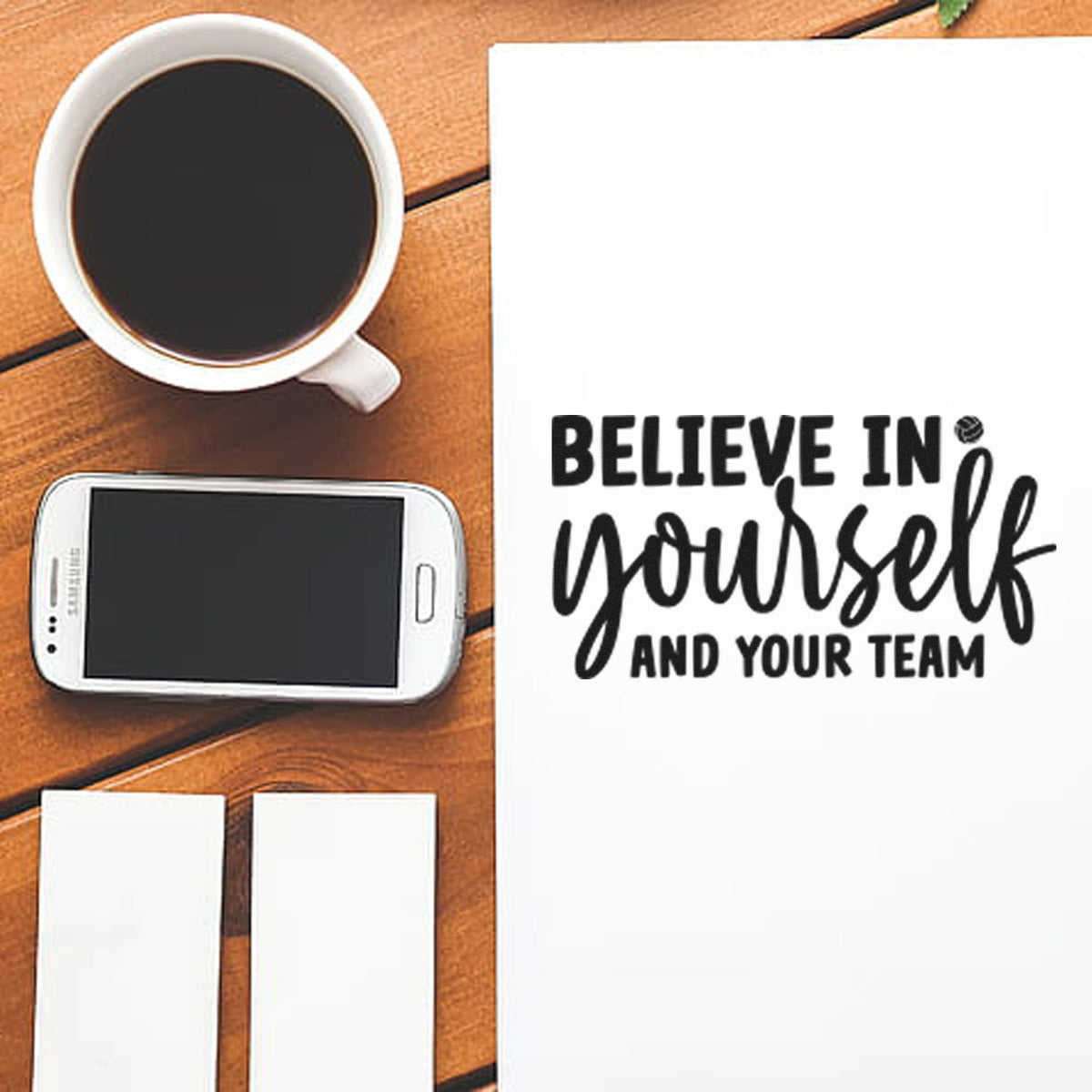 Black self-inking stamp and seal products on wood beside a coffee mug, with white print reading Believe in yourself and your team.