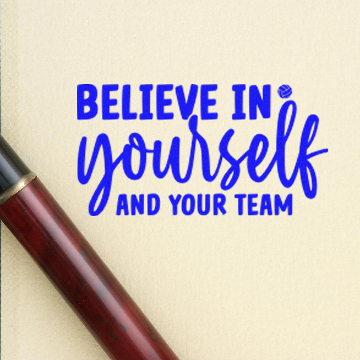 Blue rubber stamp impression reading Believe in yourself and your team on cream paper, with maroon stamp handle.