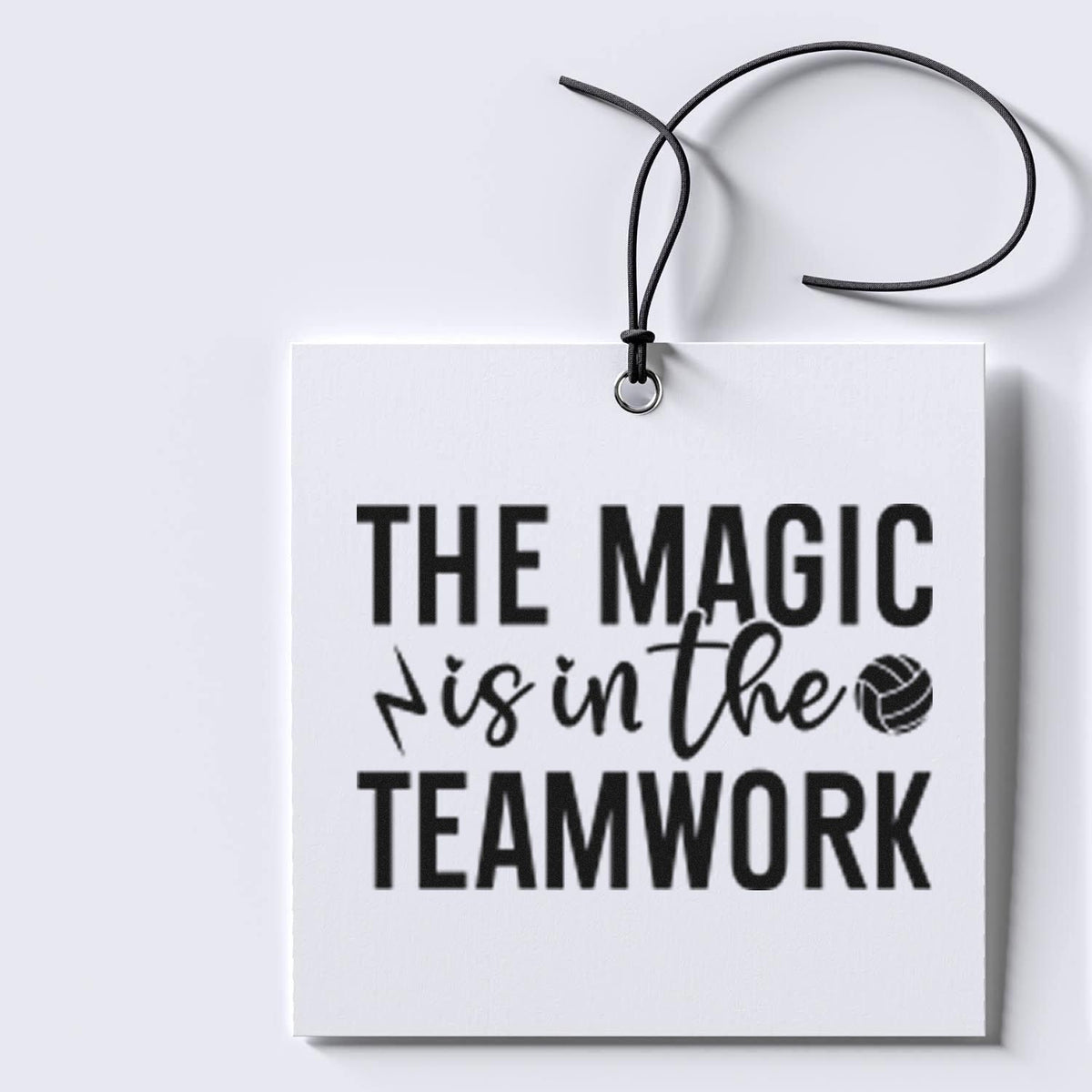 White stamp-and-seal hanging tag with black cord and ring, printed with bold black The magic is in the teamwork text.