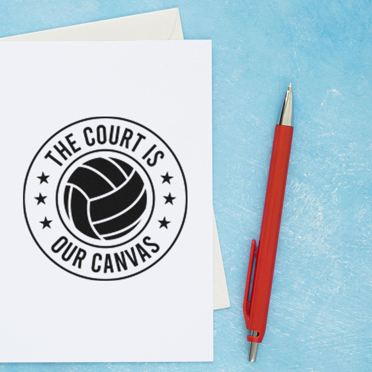 Custom stamp seal with volleyball logo and The Court Is Our Canvas on white paper, beside a red pen on a blue background.