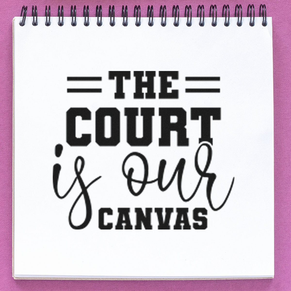 Black stamp-style seal reading The Court Is Our Canvas on a white spiral notebook with a pink background.
