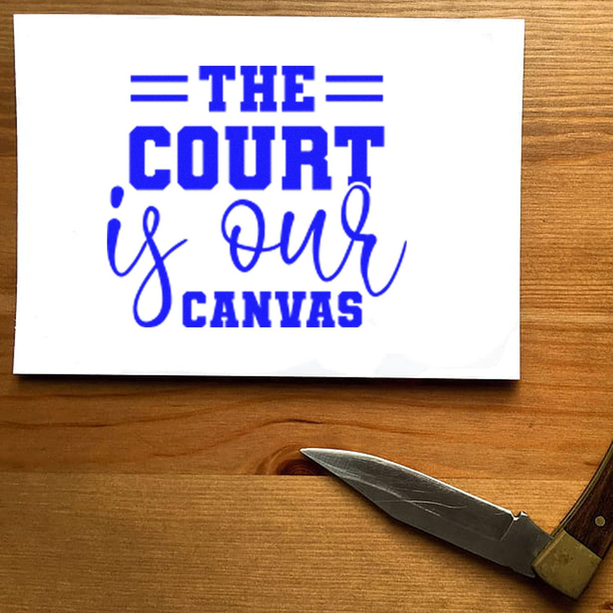 Blue custom stamp and seal reading THE COURT is our CANVAS on a white card, with a pocketknife on a wood surface.