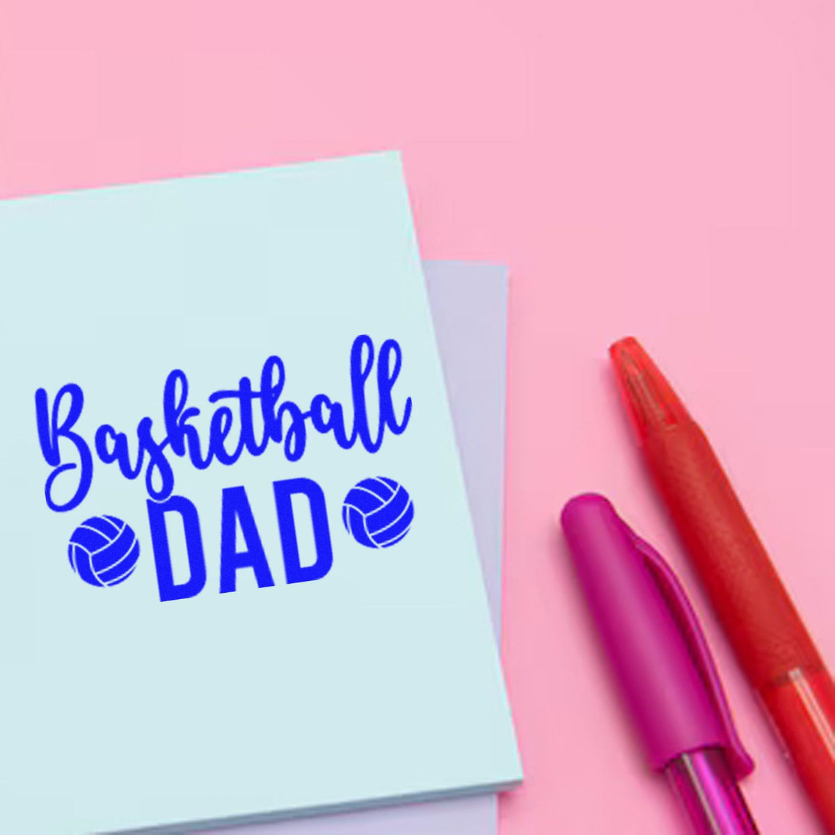 Basketball DAD stamp/seal on light blue card, with red and magenta pens on a pink background.