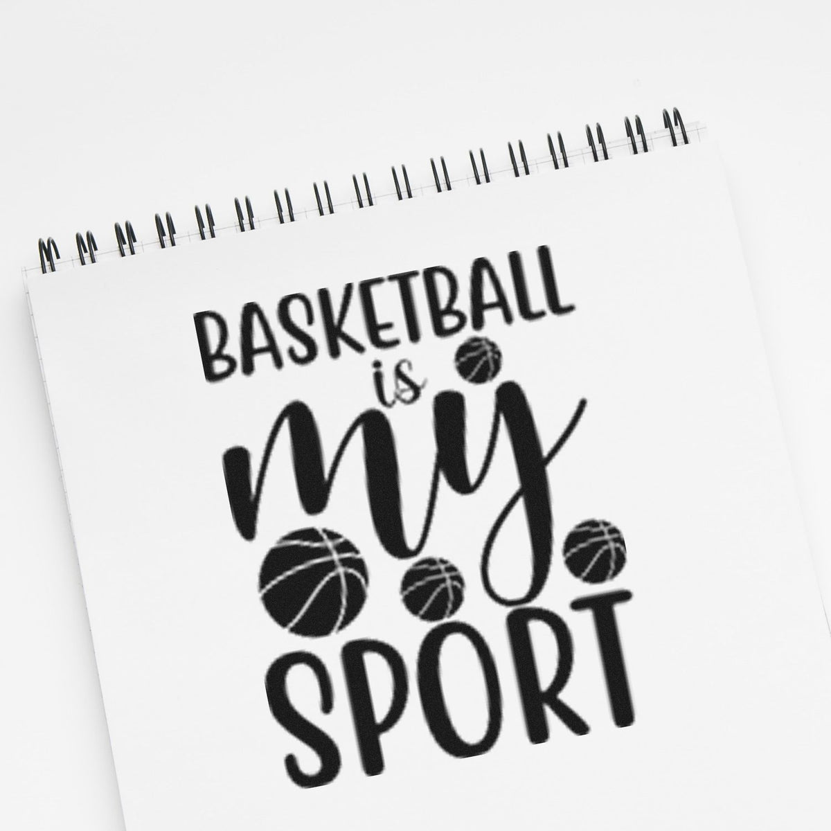 Black basketball-themed stamp design on white spiral notebook, reading Basketball is my sport with basketball icons.