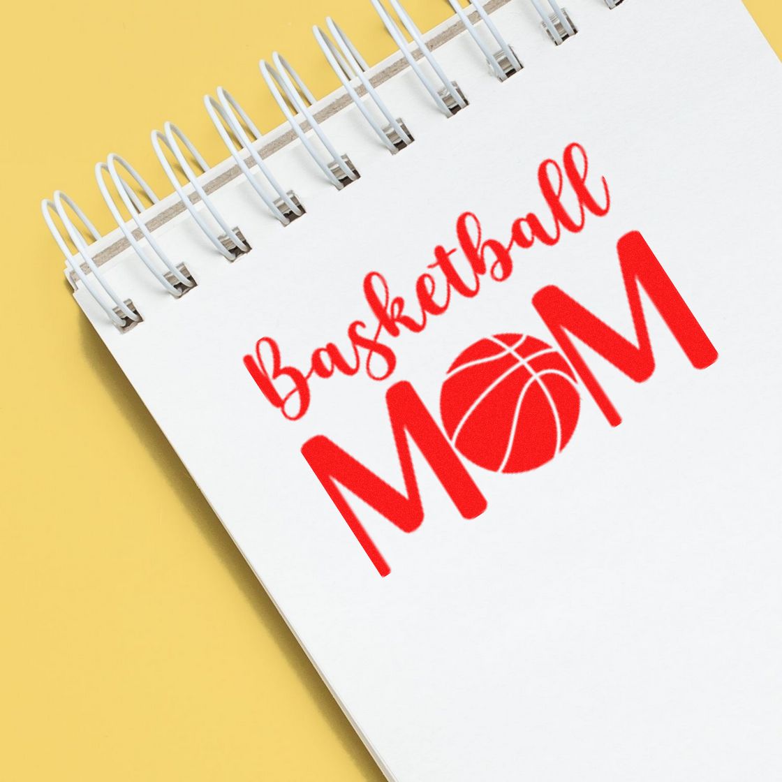 Custom red Basketball Mom stamp and seal design with basketball icon on a white spiral notebook, set against a yellow background