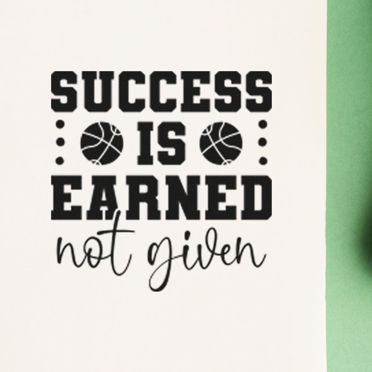 Black rubber stamp seal saying SUCCESS IS EARNED, not given with basketball icons on white paper and green edge.