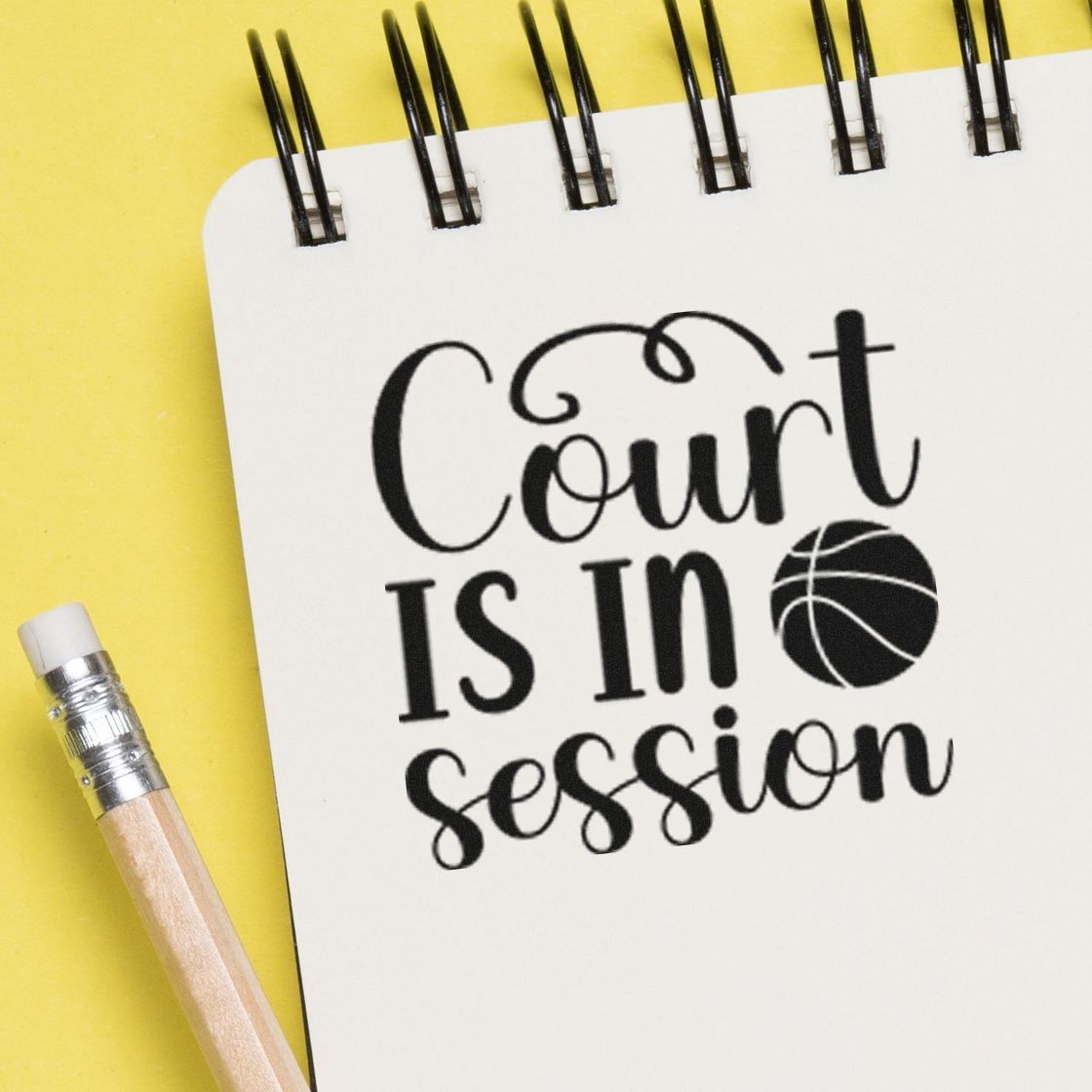 Black Court is in session stamp on white spiral notebook, with basketball icon, beside a pencil on bright yellow background.