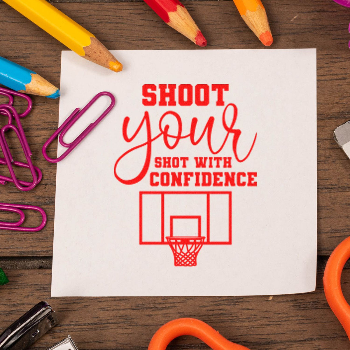 Red rubber stamp/seal on white card reads Shoot your shot with confidence, with basketball hoop, pencils, and purple paper clips.