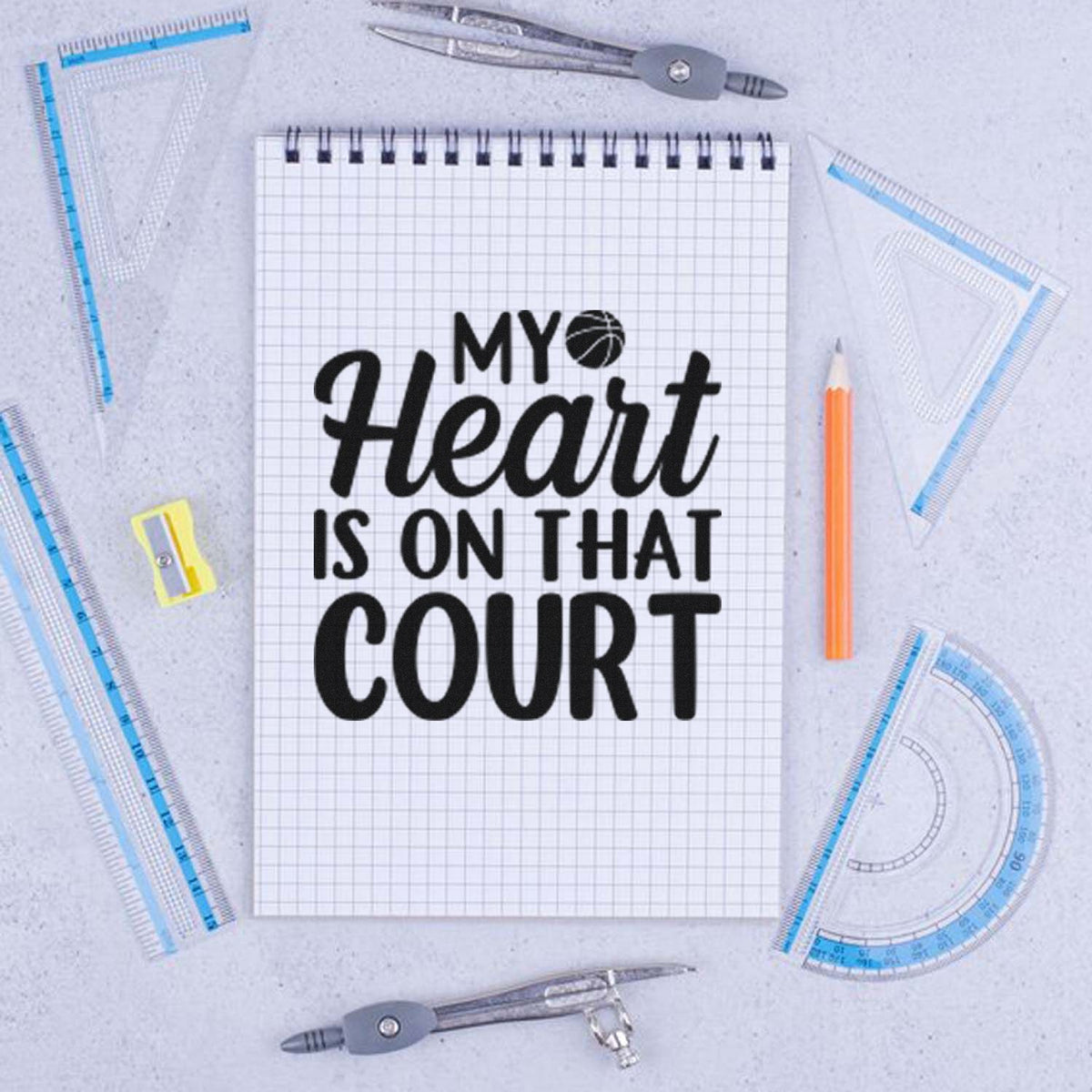Custom stamp and seal design on graph notebook with black basketball text, blue rulers, gray compass, and orange pencil.