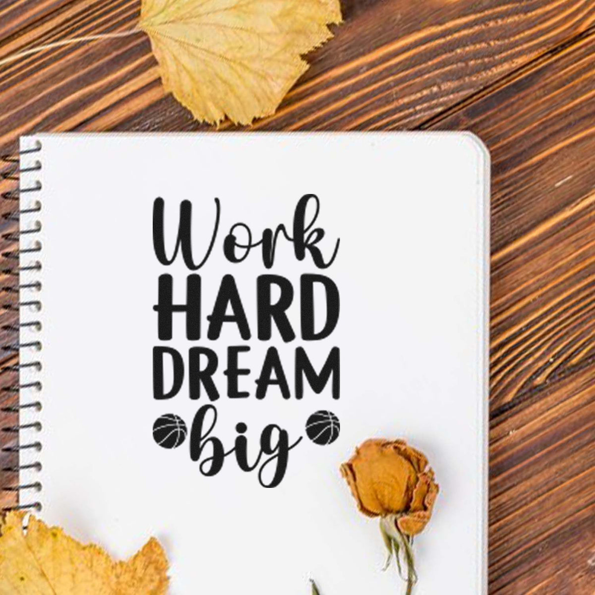 White notebook stamp and seal design with black Work Hard Dream Big lettering, on rustic wood with yellow leaves.