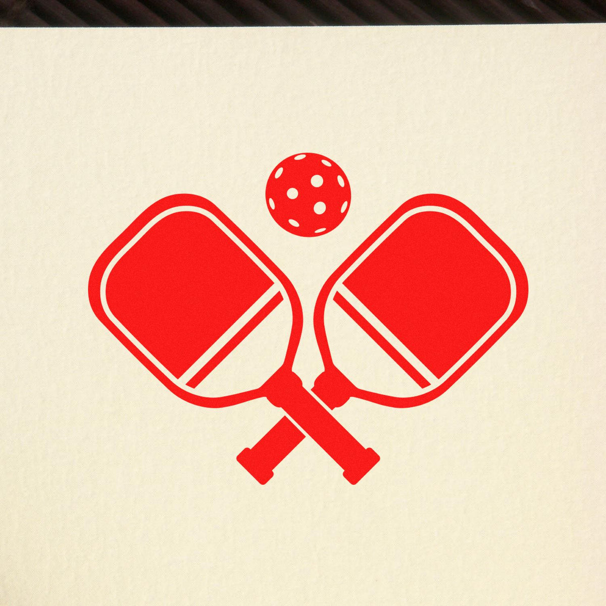 Red stamp seal with crossed pickleball paddles and polka-dot ball on a cream background
