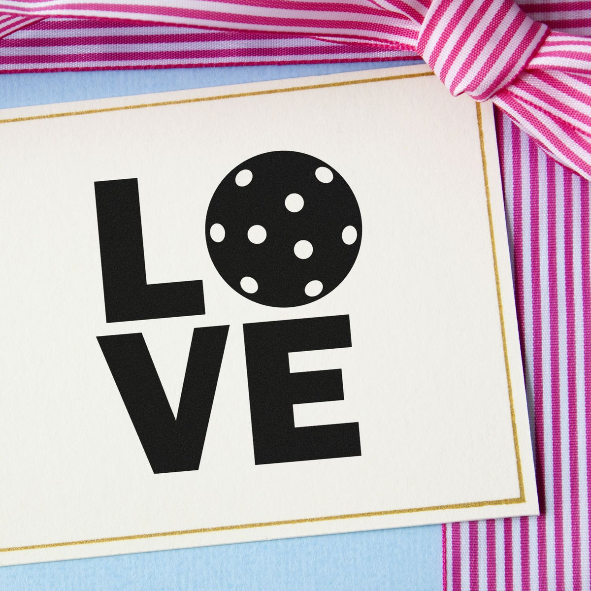 Black LOVE stamp/seal on white card with gold border, polka-dot O, and pink striped ribbon.